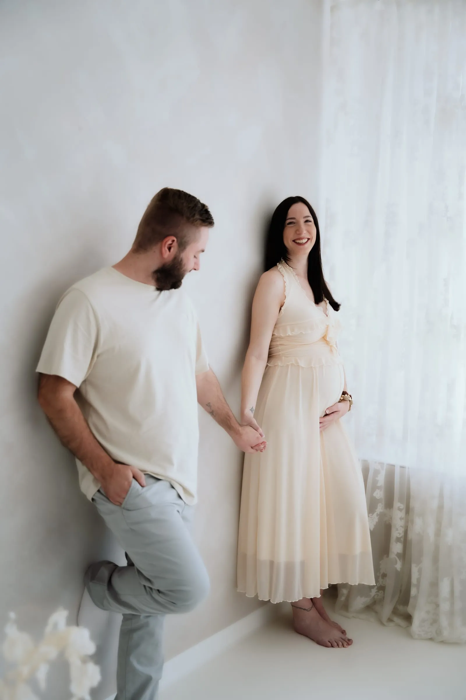 Werdende Eltern im hellen Studio, sie im cremefarbenen Kleid