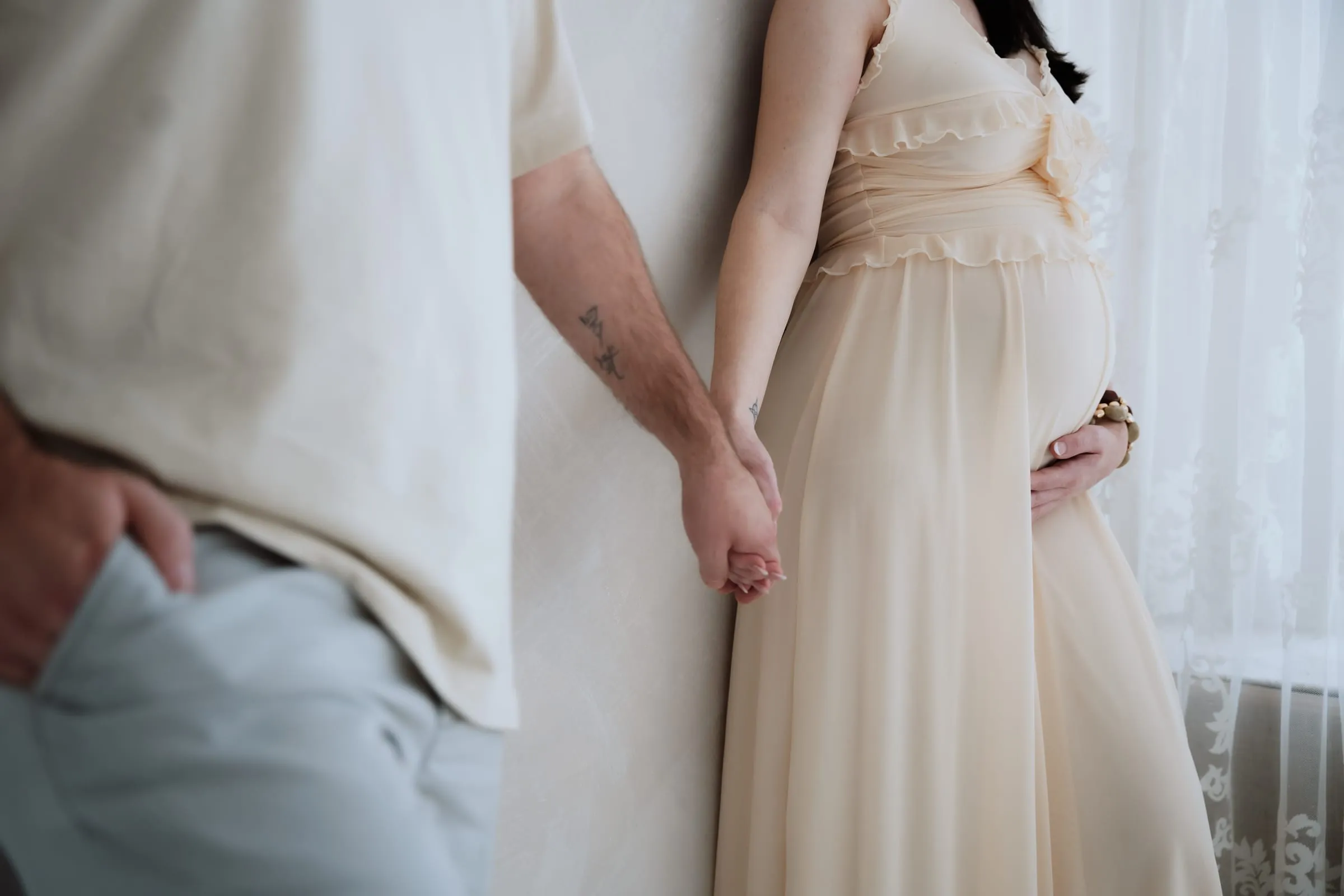 Seine Hand an ihrem Babybauch, beide in Creme