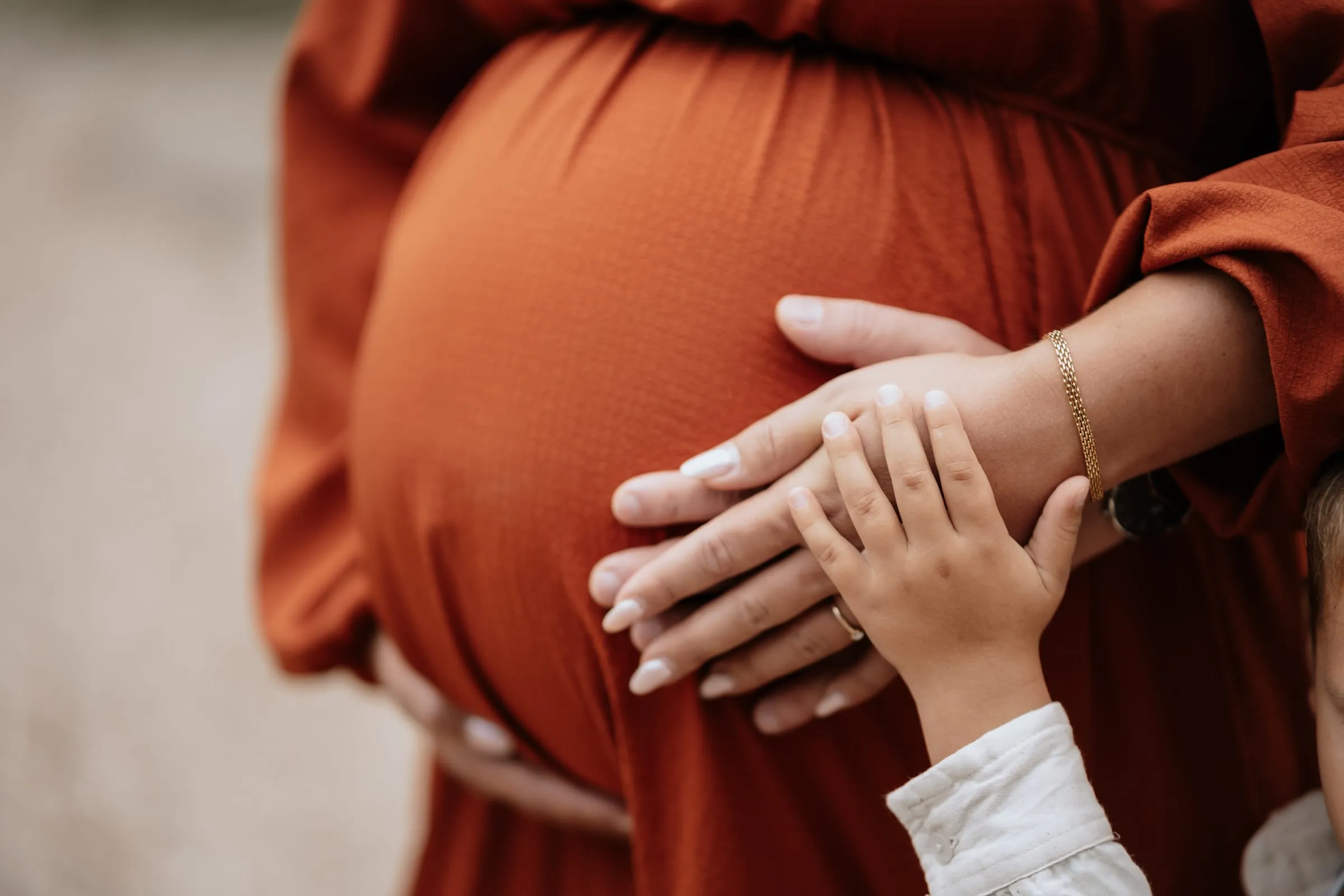 Hände auf dem rostroten Kleid über dem Bauch, auch eine kleine Kinderhand