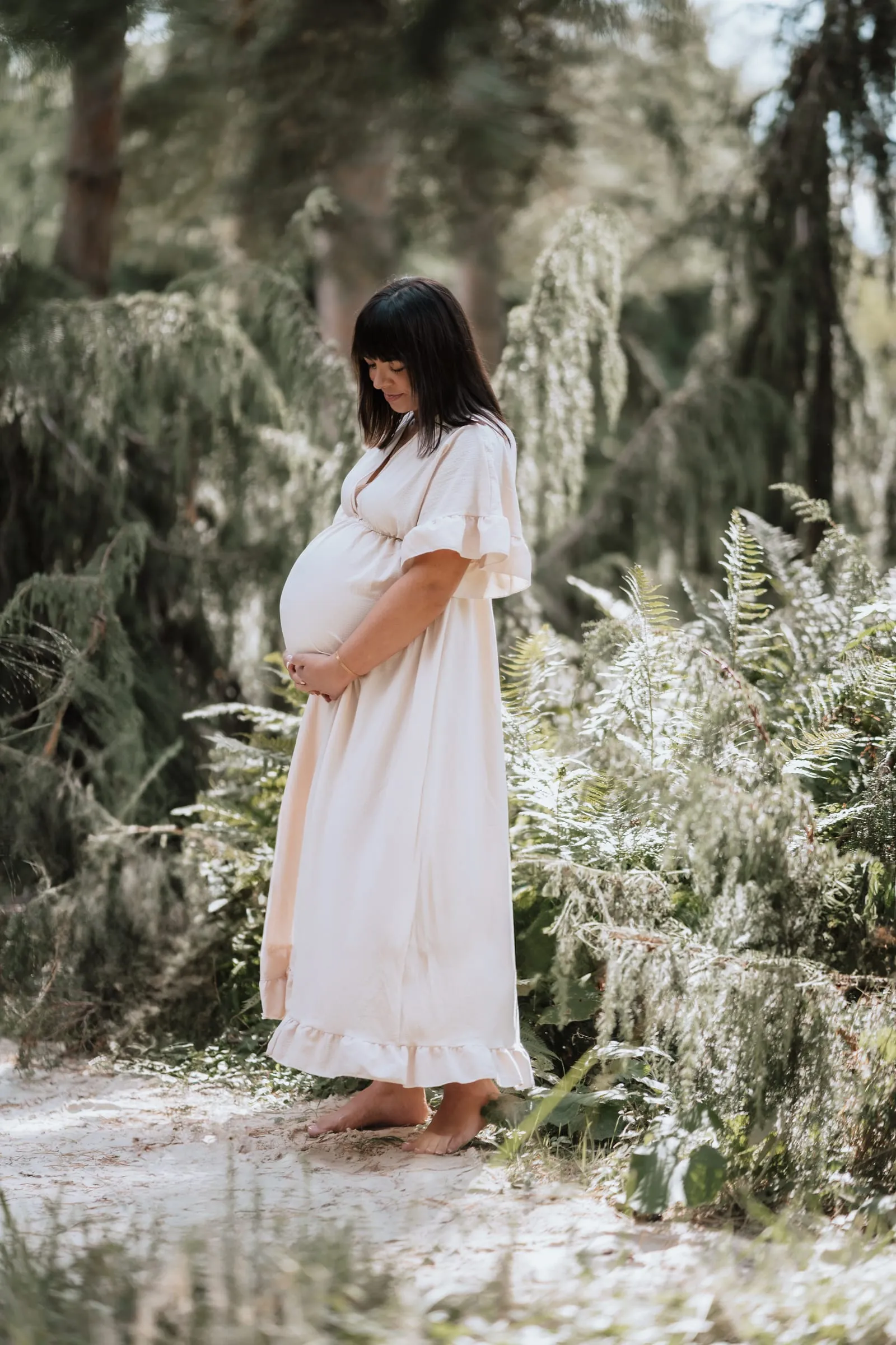 Schwangere im weißen Kleid zwischen Sträuchern