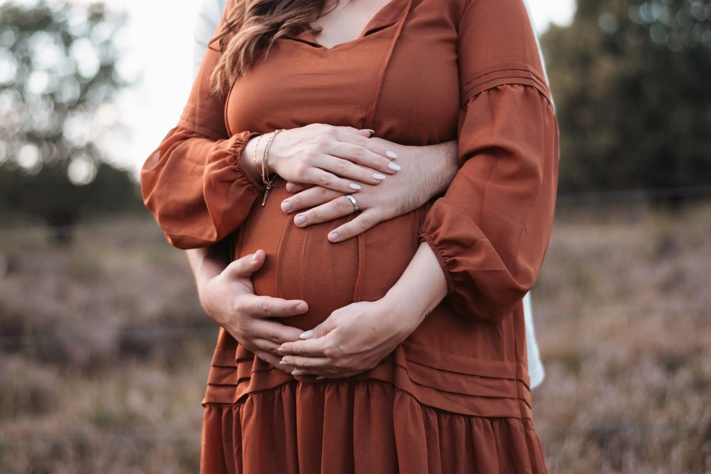 Seine Hände umfassen ihren Bauch im rostroten Kleid