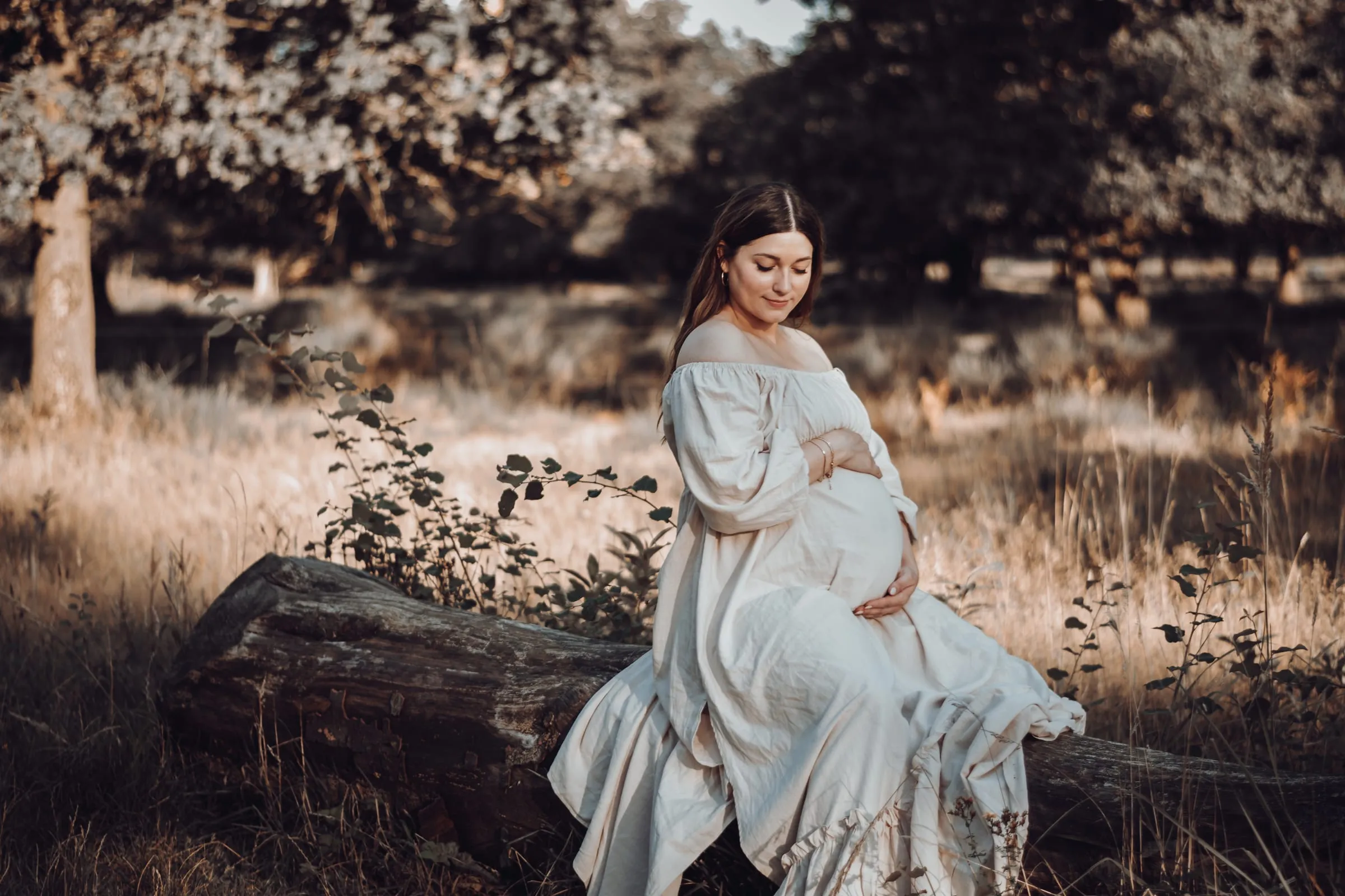 Sie sitzt im weißen Kleid auf einem Baumstamm