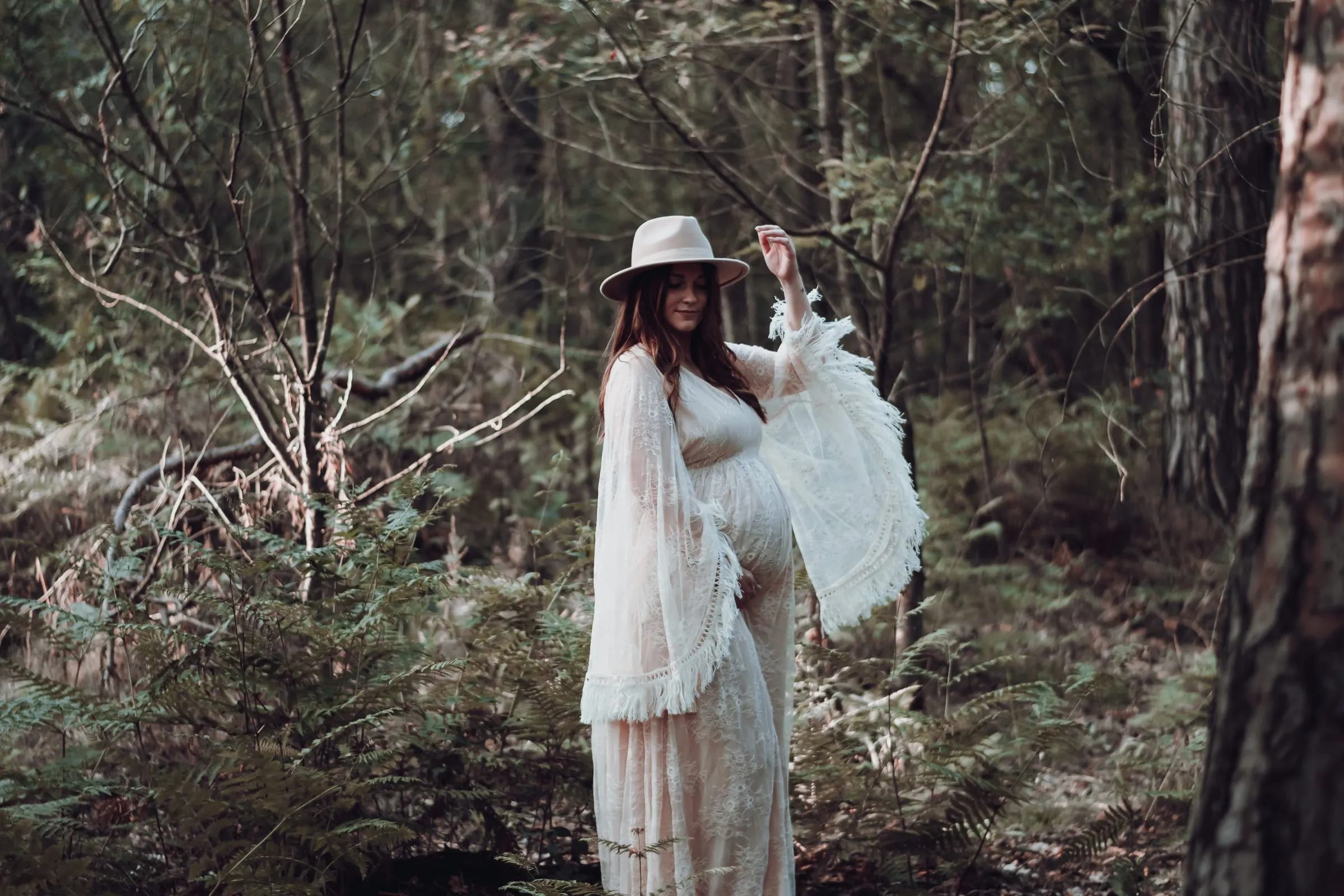 Mit Hut und Spitzenkleid im Wald, der Ärmel weht
