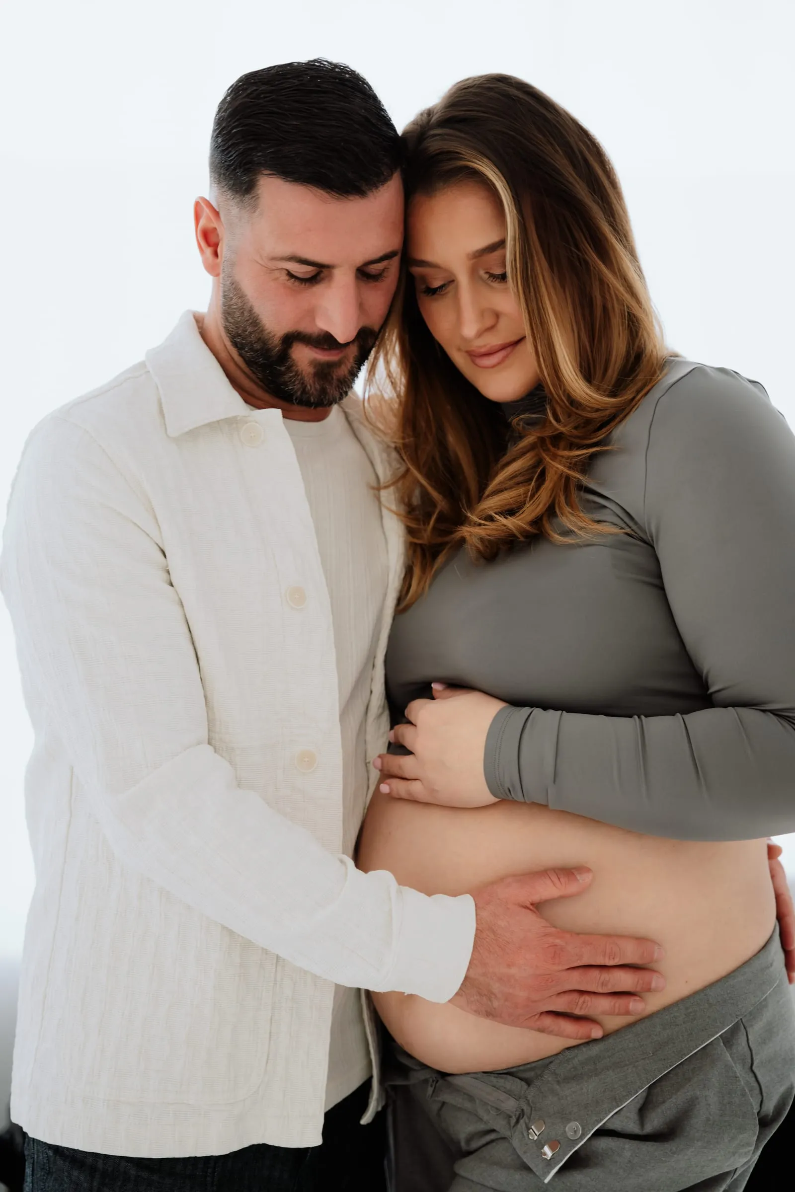 Das Paar im Studio, er umarmt sie, der Babybauch ist frei