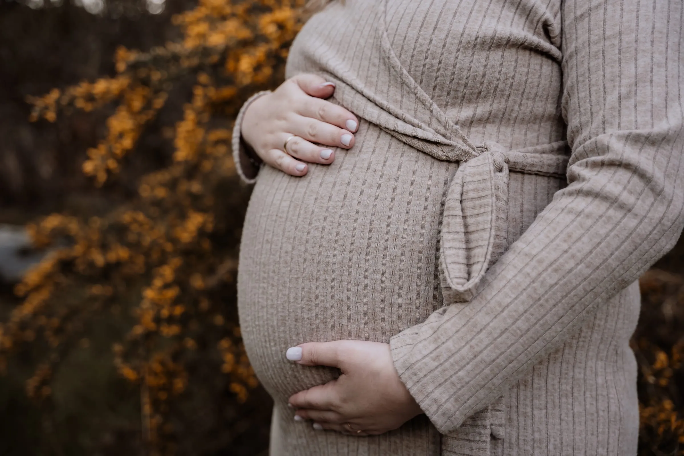 Babybauch im Strickkleid vor herbstlichem Laub