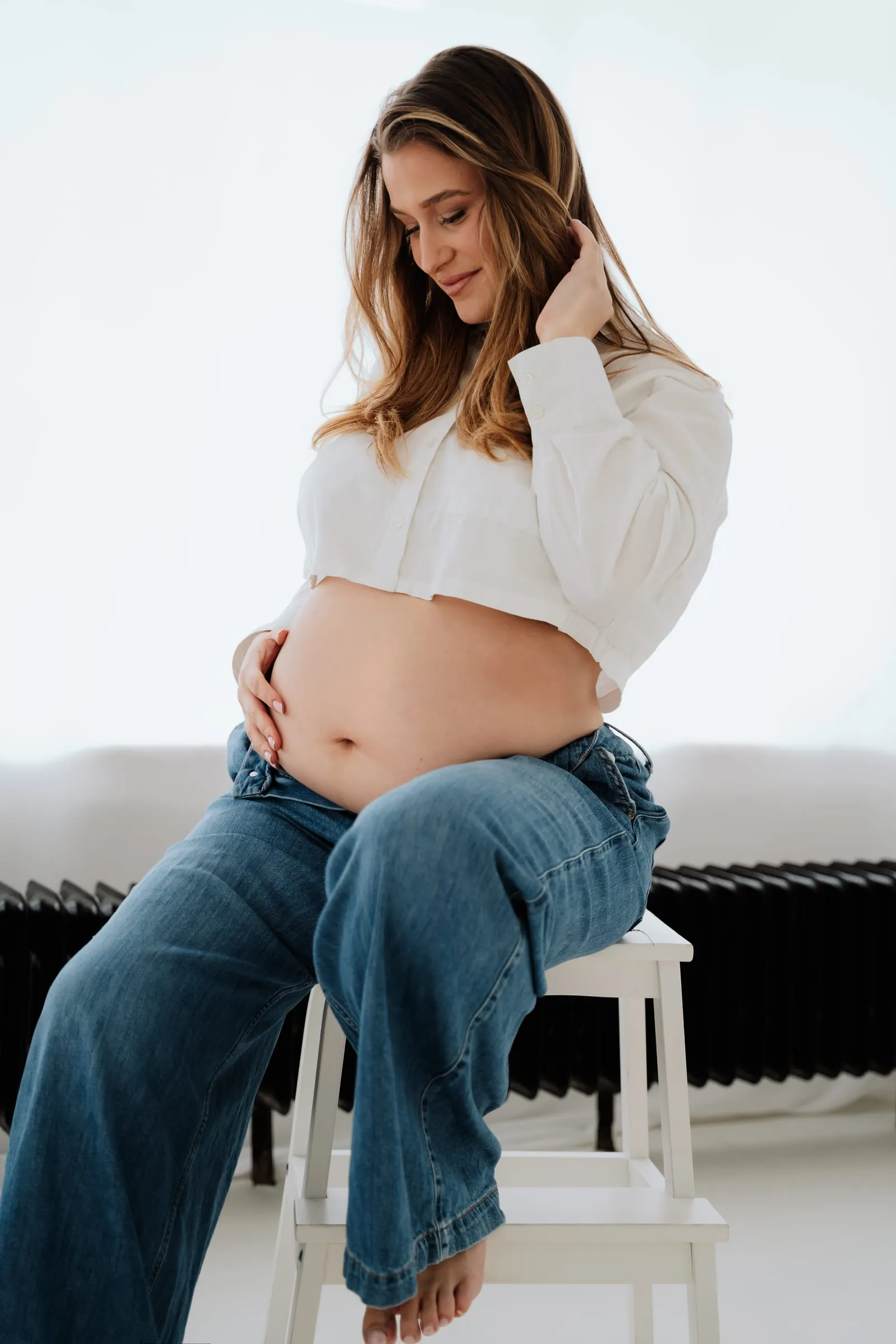 Die Schwangere sitzt auf einem Hocker, die Hände am Bauch