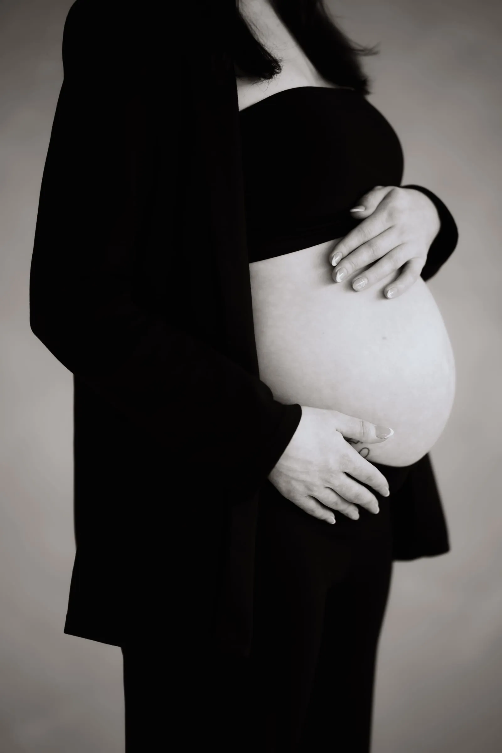 Babybauch im Profil, eine Hand darauf, daneben der dunkle Blazer, in Schwarzweiß