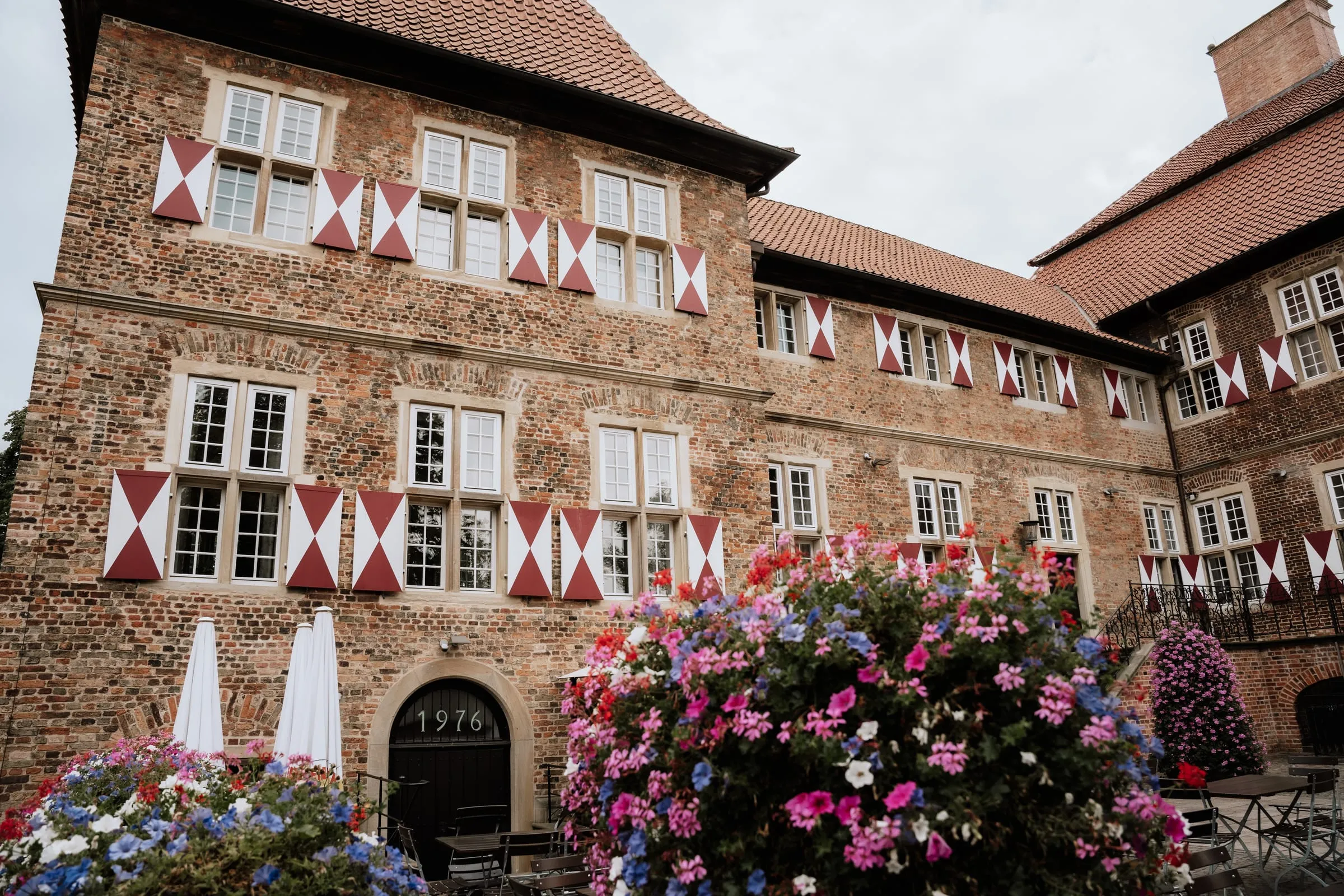 Backsteinschloss mit Wimpelketten, davor blühende Blumenkästen