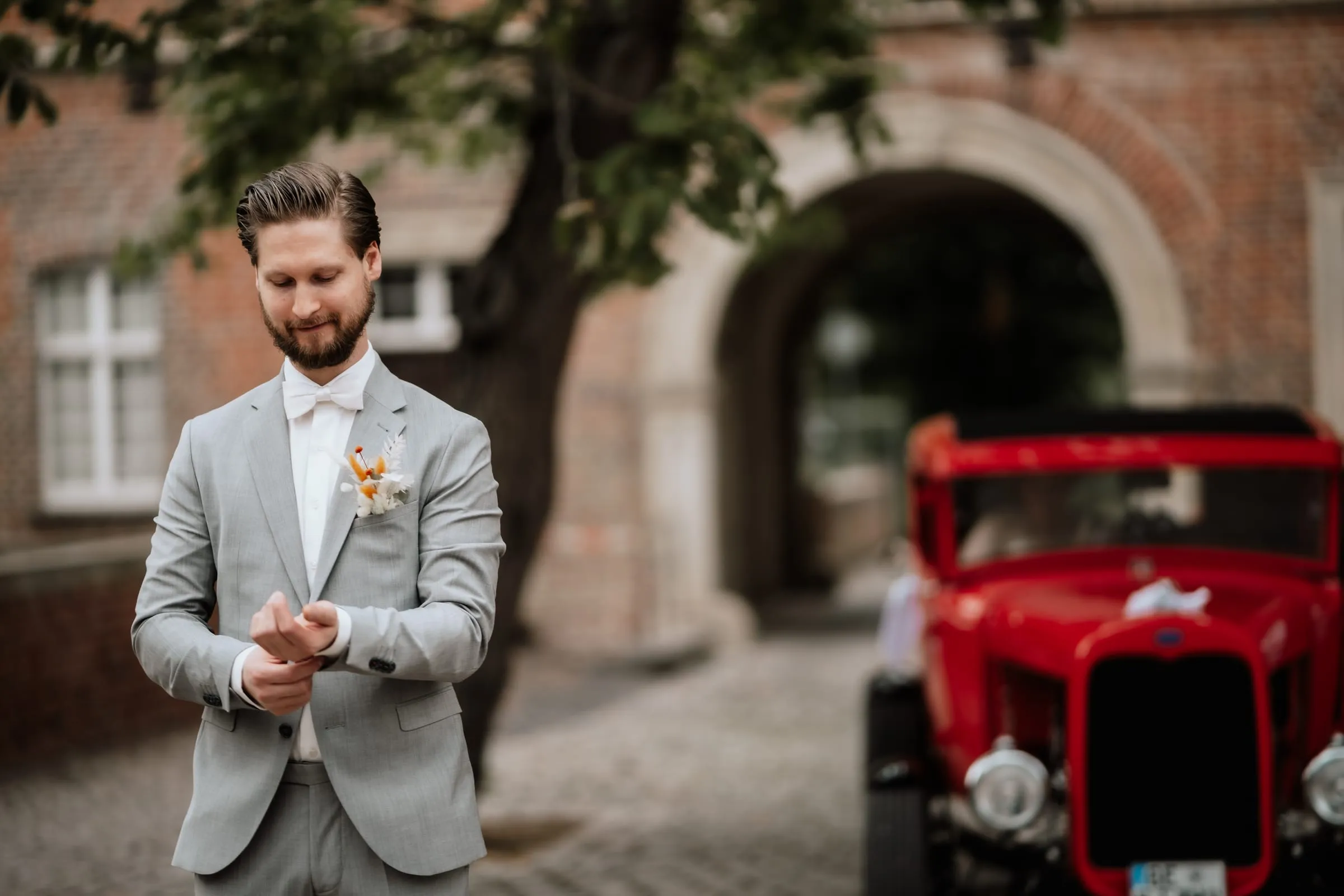 Der Bräutigam vor einem Torbogen, daneben ein roter Oldtimer