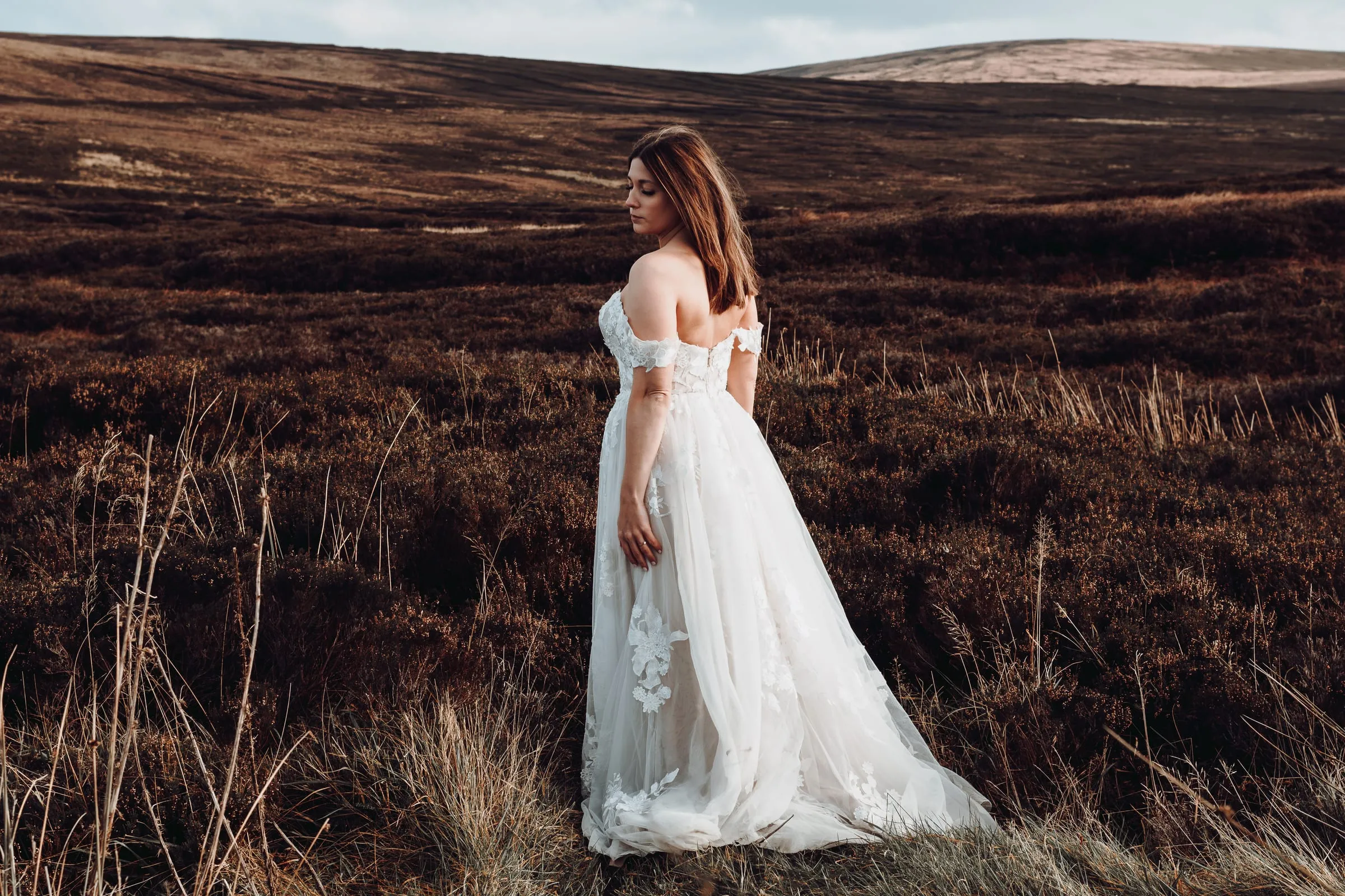 Die Braut im Spitzenkleid steht allein in der weiten Heide