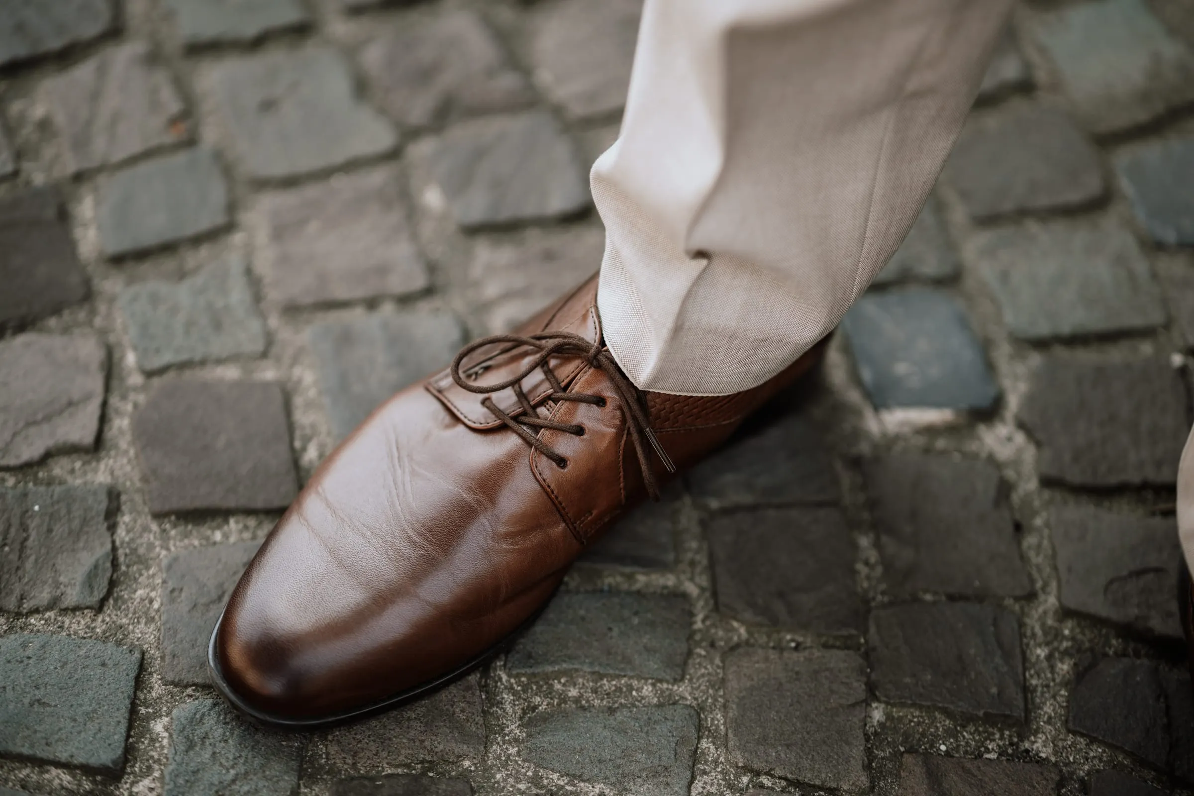 Braune Schnürschuhe des Bräutigams auf Kopfsteinpflaster