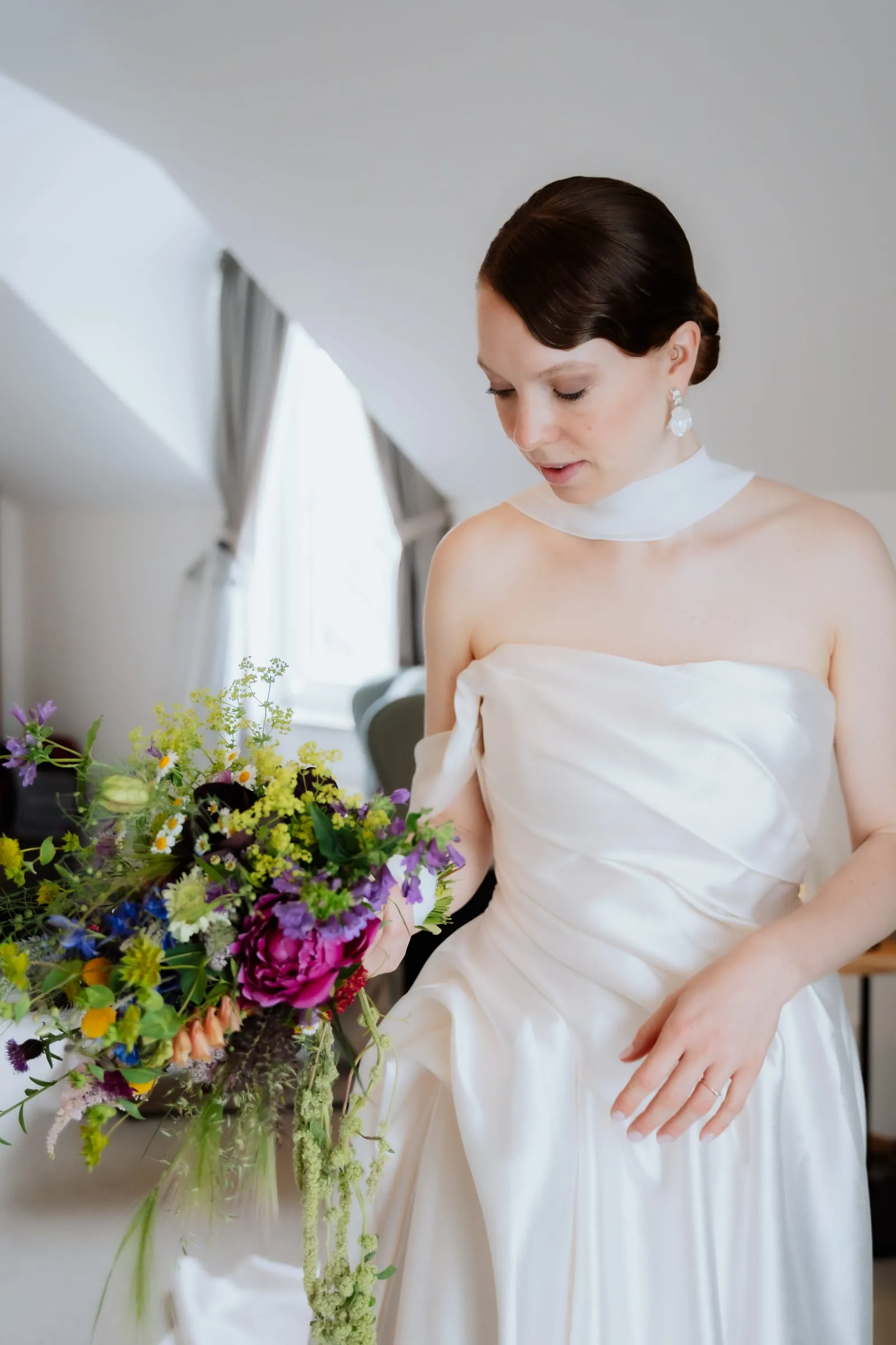Die Braut im Kleid mit buntem Strauß am Fenster