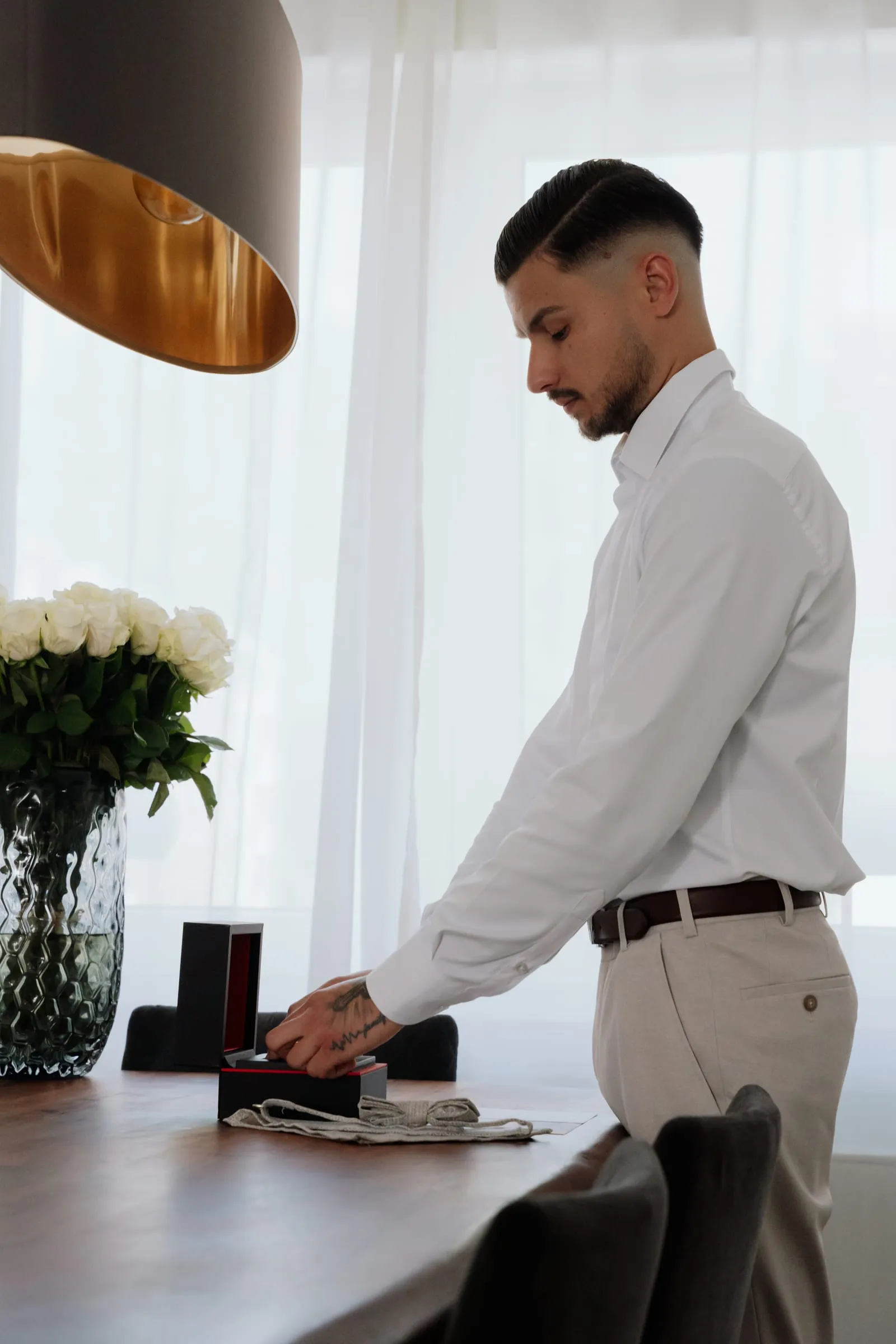 Der Bräutigam beim Anziehen am Tisch, daneben Blumen