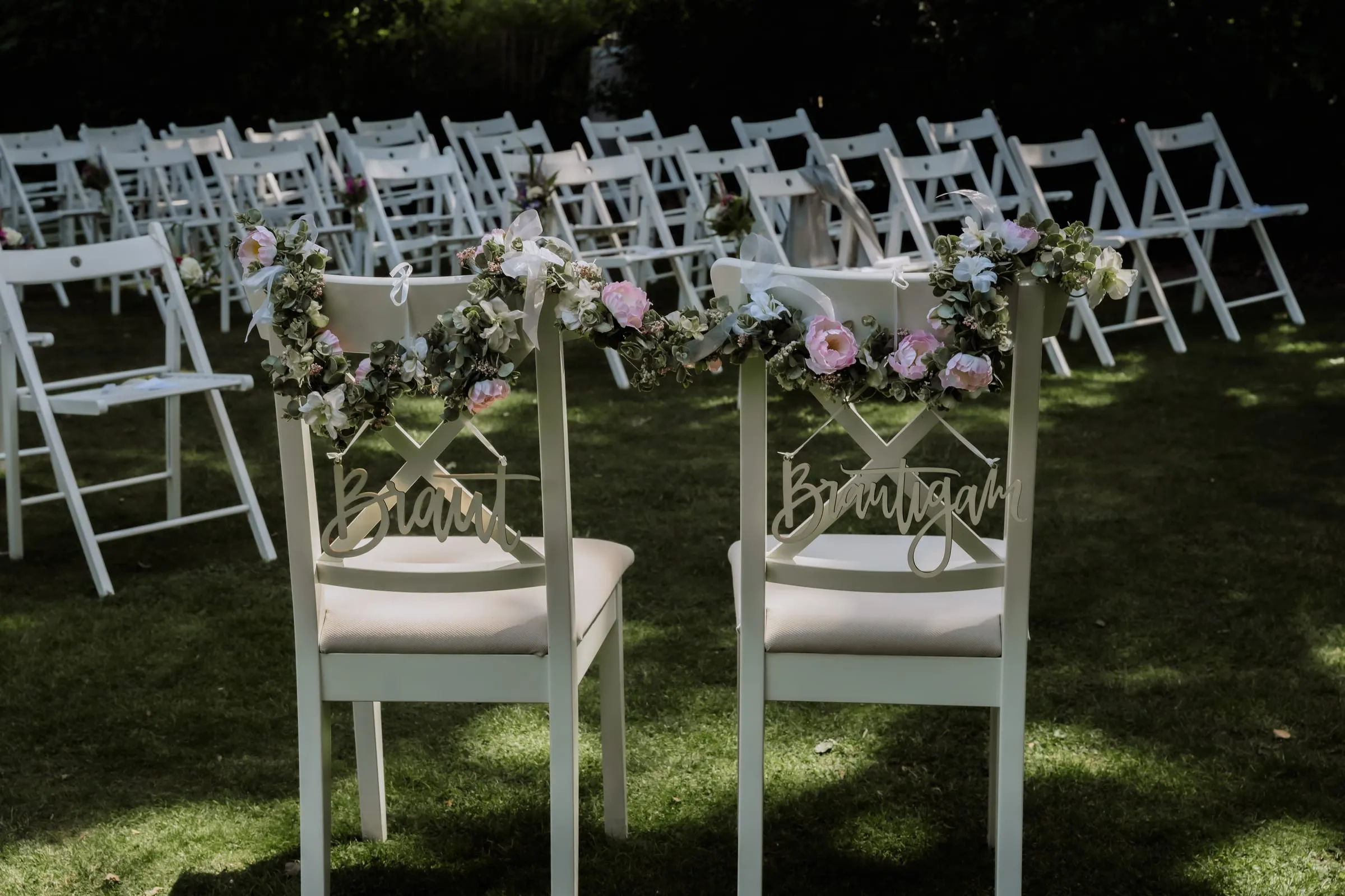 Weiße Stühle mit Blumenschmuck für die Trauung