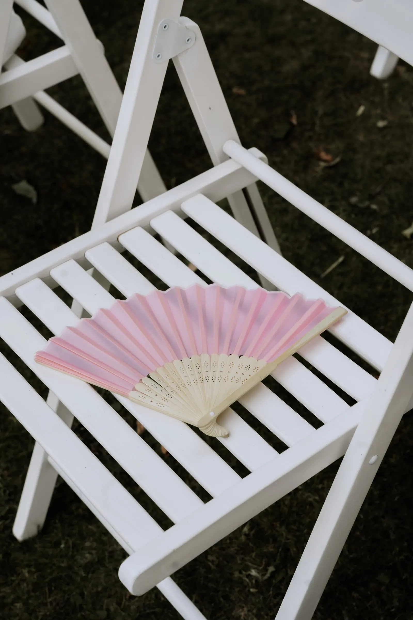 Ein rosa Fächer liegt auf einem weißen Stuhl