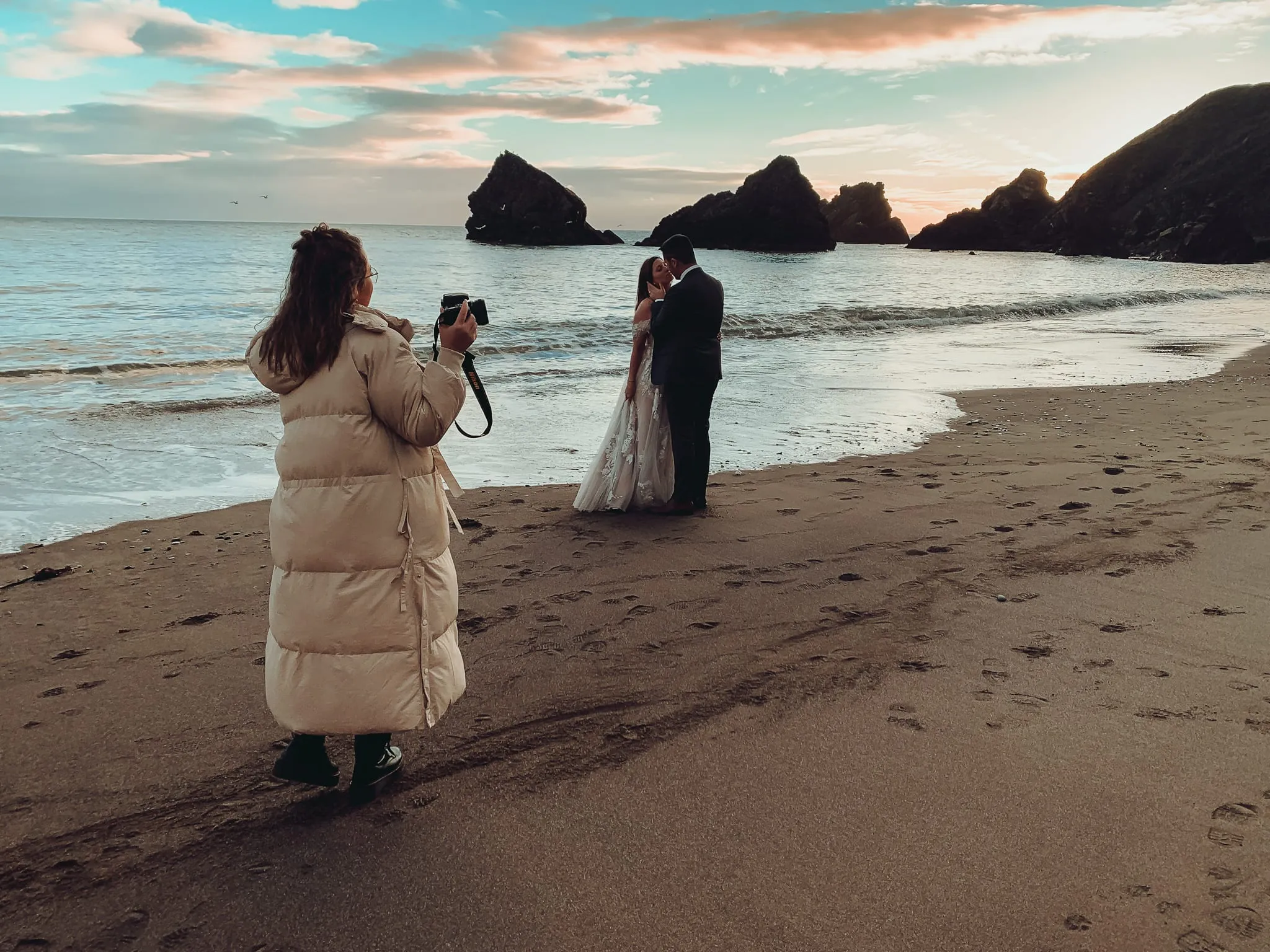 Hinter den Kulissen am Strand: Die Fotografin mit Kamera, das Brautpaar an der Wasserlinie