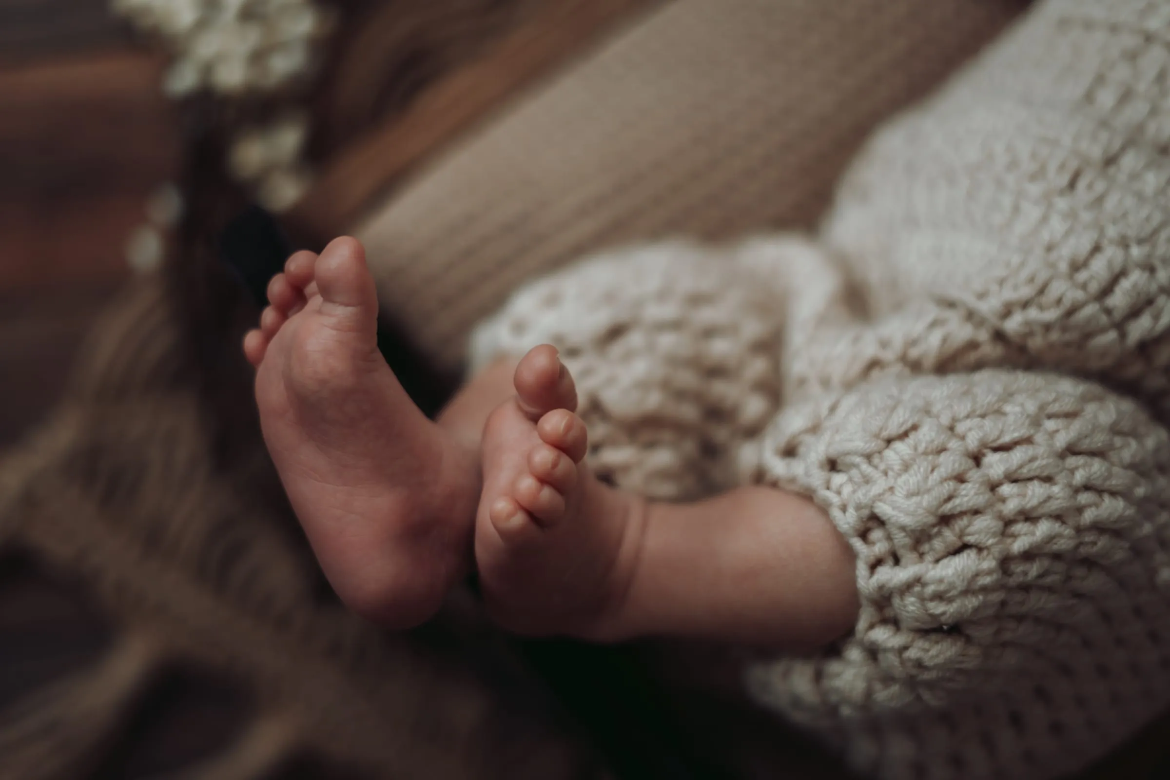 Winzige Babyfüße im cremefarbenen Strickanzug, daneben Trockenblumen