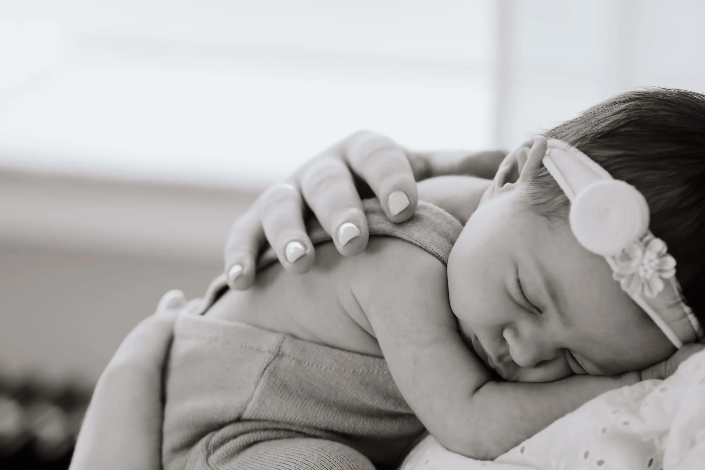 Die Mutter beugt sich über ihr schlafendes Baby mit Haarband, in Schwarzweiß