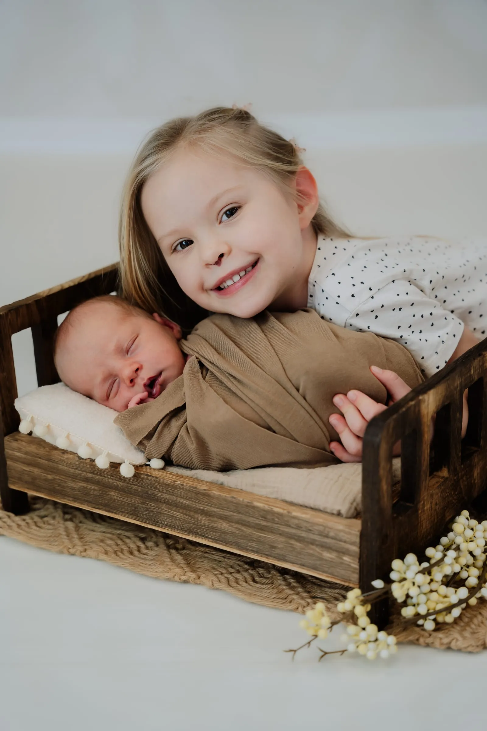 Die große Schwester lacht neben dem schlafenden Baby im Holzbett