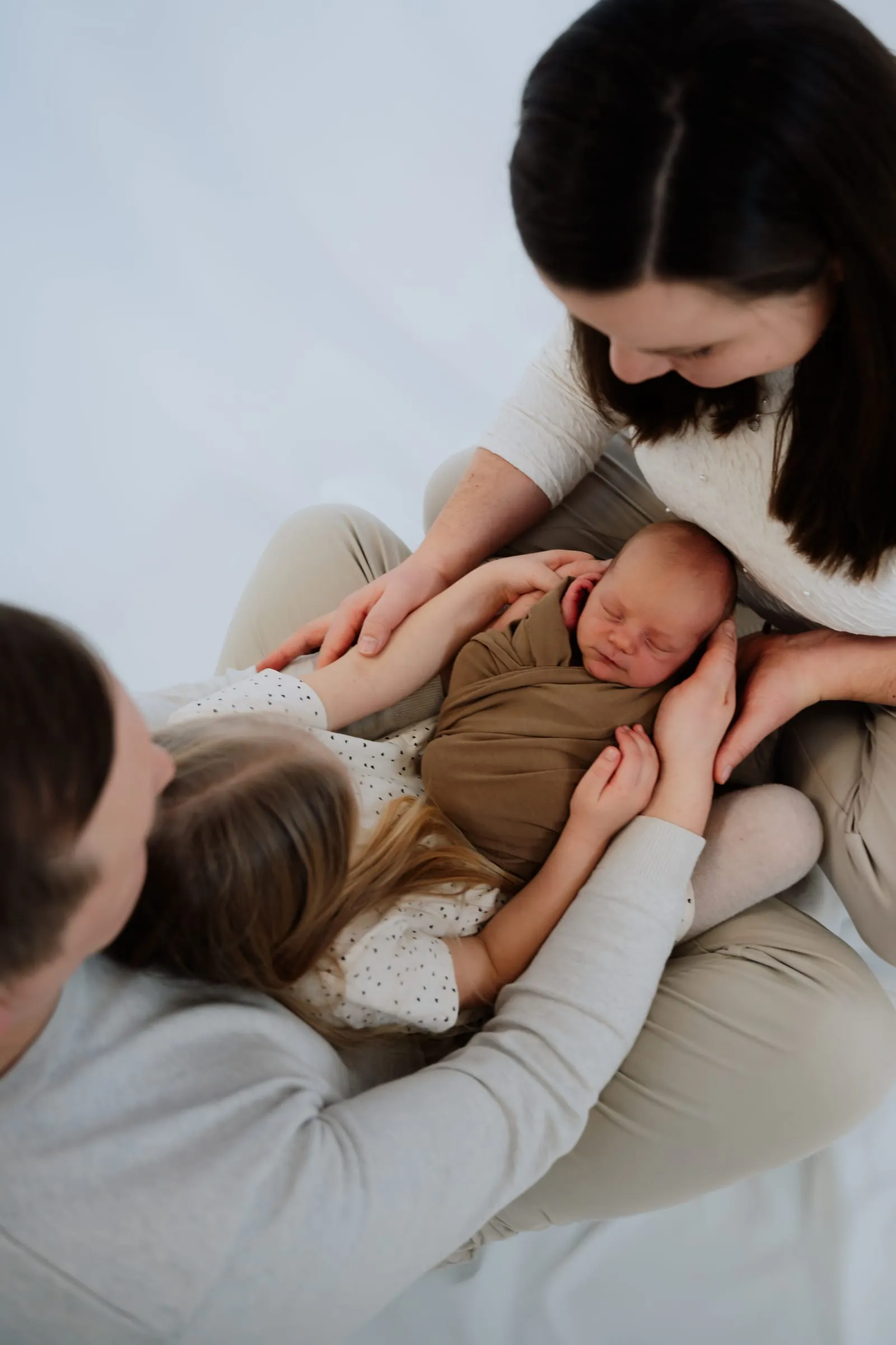 Mutter und Geschwisterkinder halten gemeinsam das Neugeborene