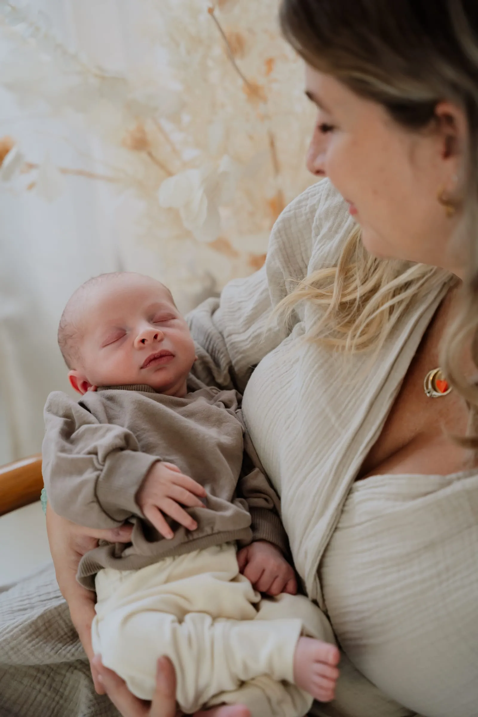 Die Mutter blickt auf ihr Baby in ihren Armen, dahinter Trockenblumen