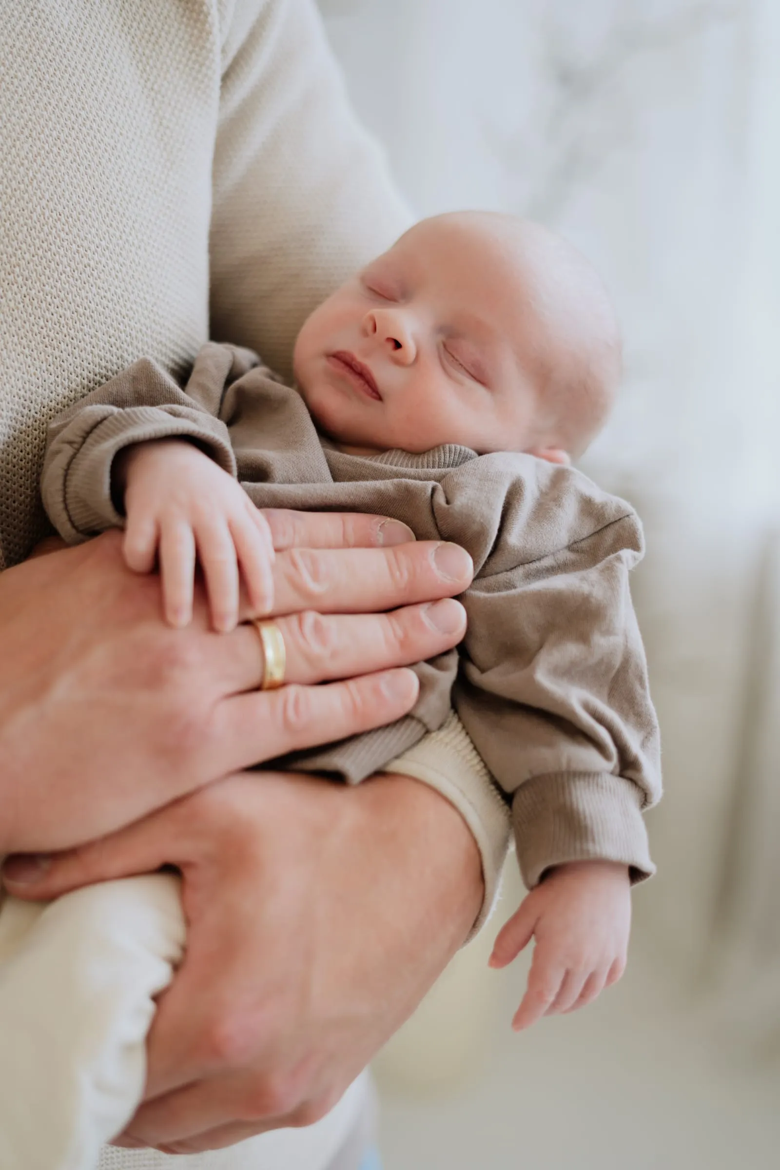 Das Baby liegt schlafend in den Händen seines Vaters
