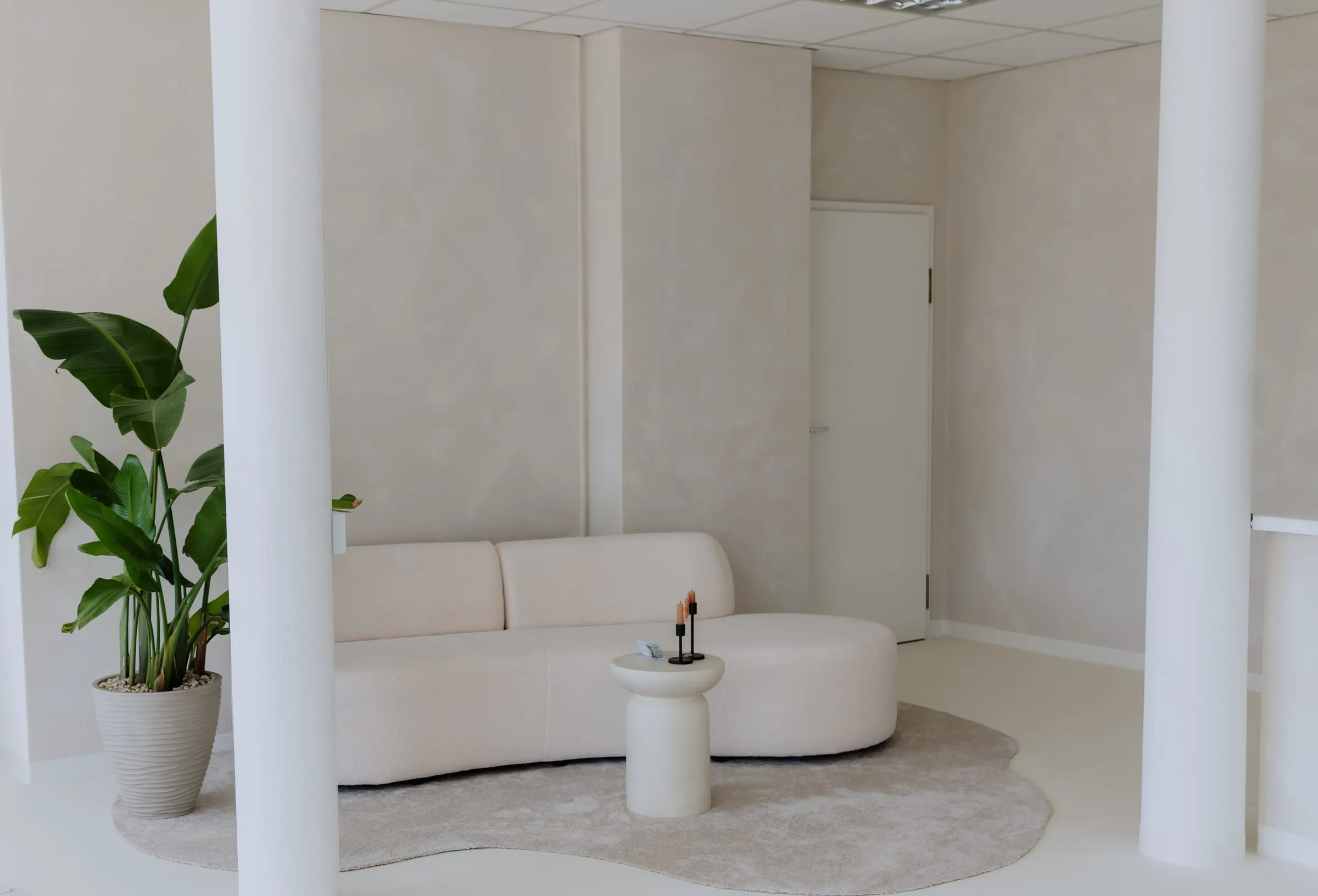 Wartebereich im Studio mit geschwungenem Bouclé-Sofa, Beistelltisch mit Kerzen und großer Zimmerpflanze
