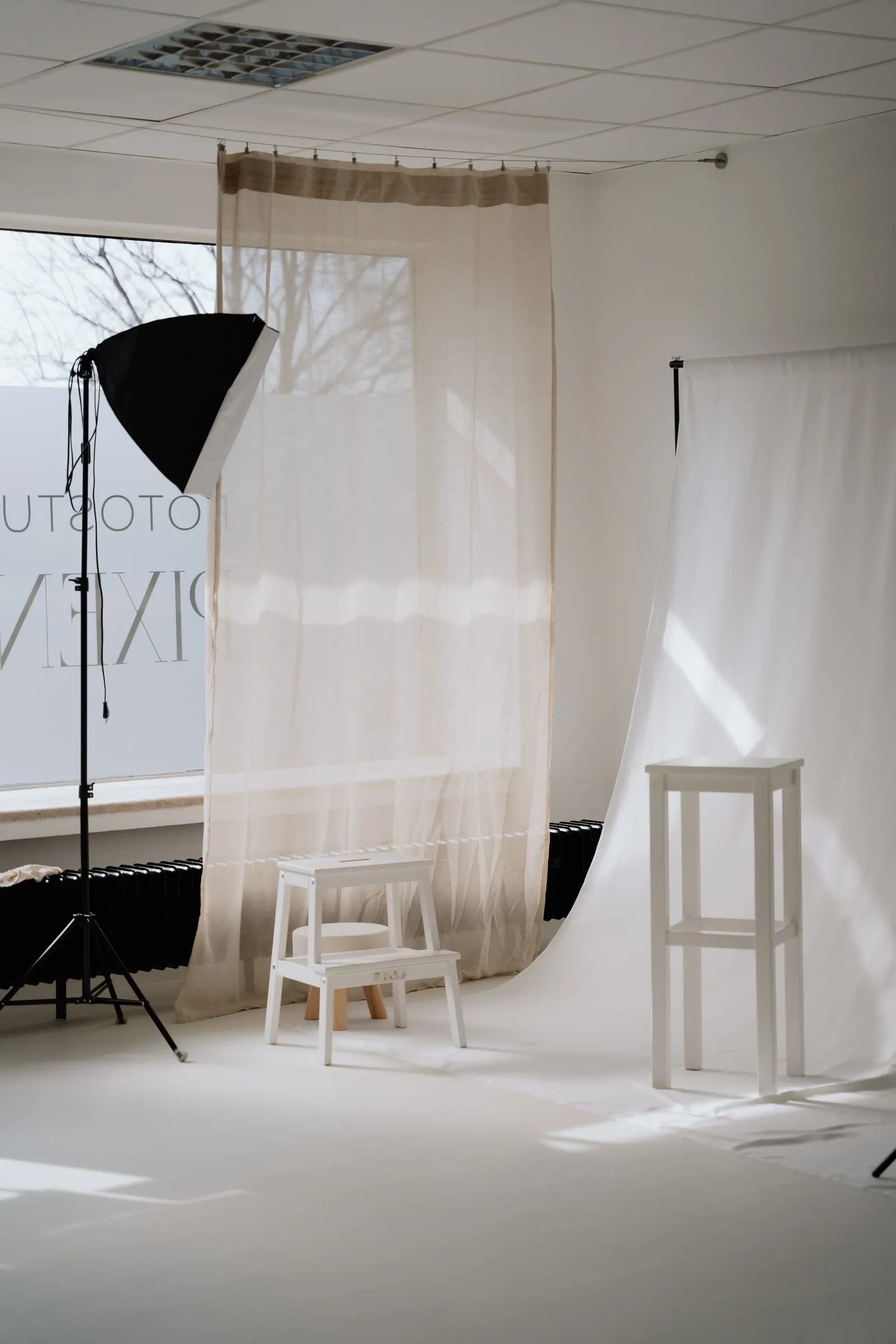 Shootingecke im Studio mit Softbox, hellem Vorhang, weißem Hintergrundstoff und Hockern