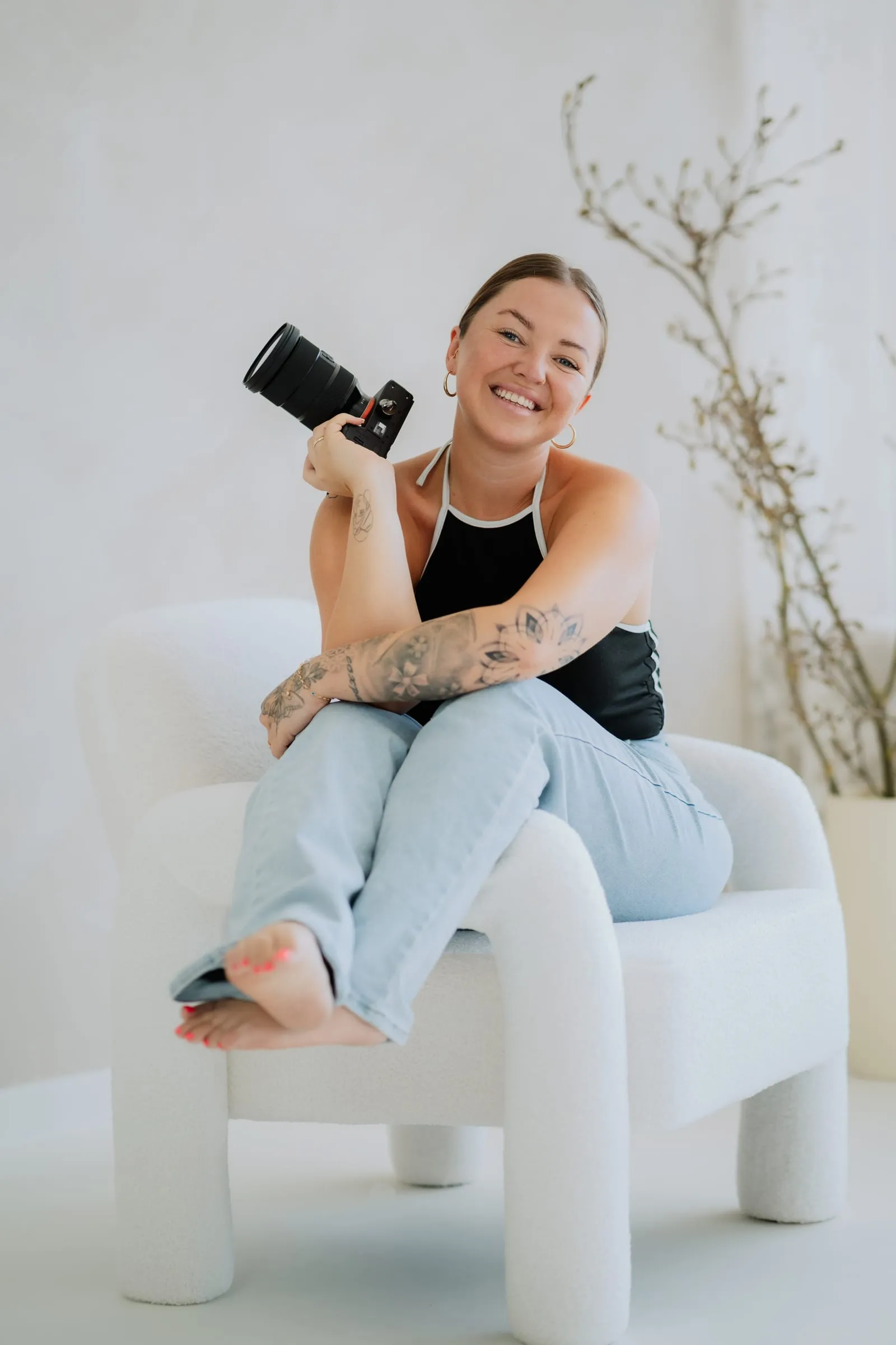Xenia sitzt mit Kamera auf einem hellen Sessel in ihrem Fotostudio