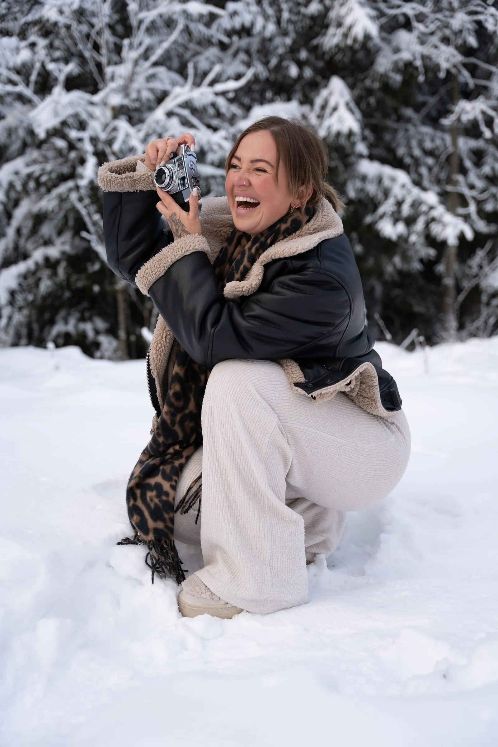 Xenia hockt lachend im Schnee und fotografiert mit einer alten Kamera